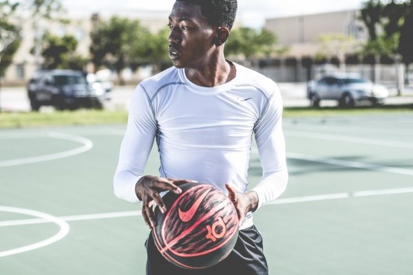 man wearing white Nike sweatshirt holding basketball ball standing on the court