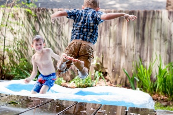 Clothed child jumping from a wooden platform into an inflatable pool where another child is playing
